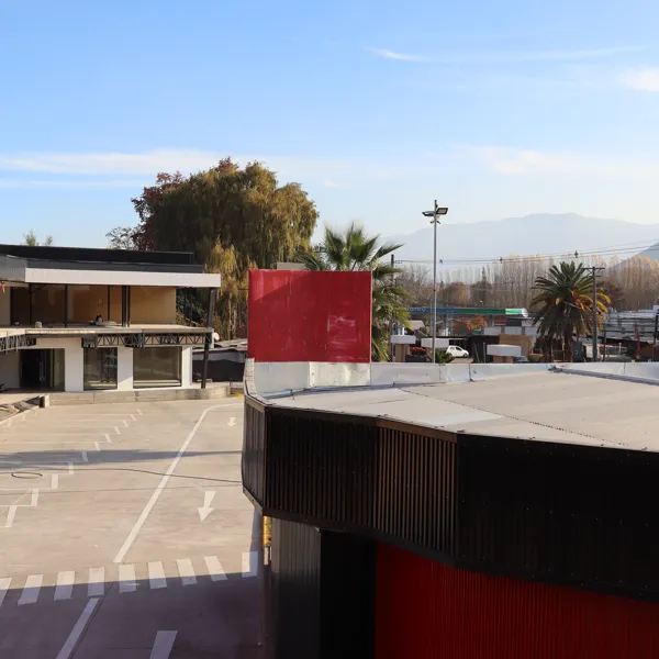 Plaza con estacionamiento demarcado, columnas rojas y cordillera