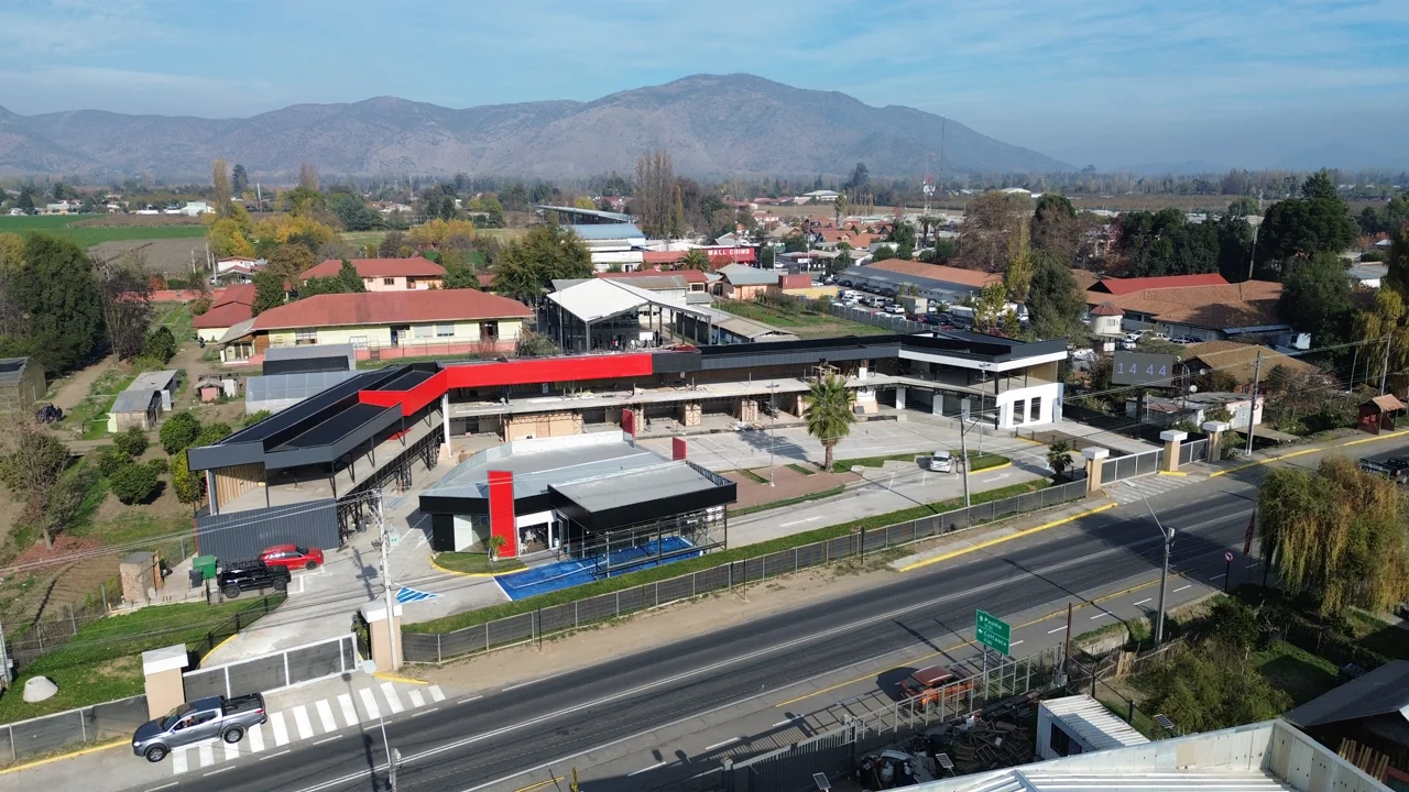 Open Boulevard Coltauco al atardecer — locales con techo rojo, detalle curvo de paneles negros con interior iluminado y parking accesible